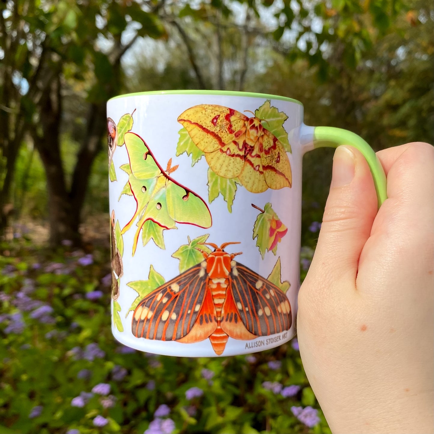 Mug with moth illustrations held by a hand in a natural setting