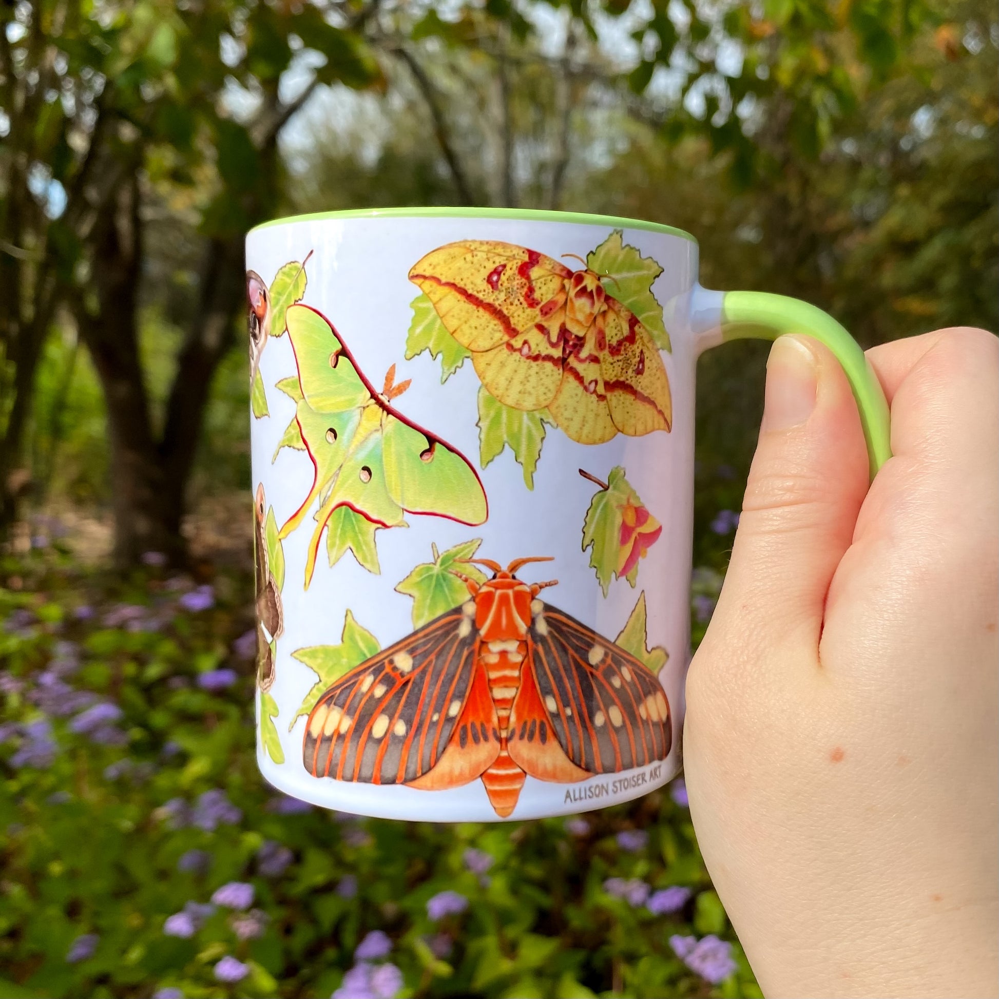 Mug with moth illustrations held by a hand in a natural setting