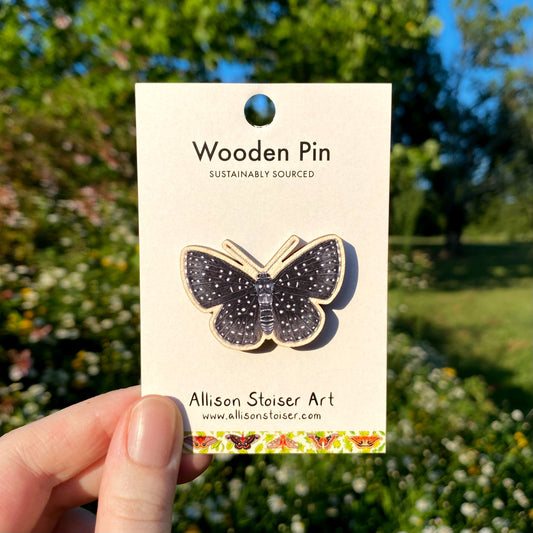 Starry night metalmark wooden pin on a card held in front of a garden background