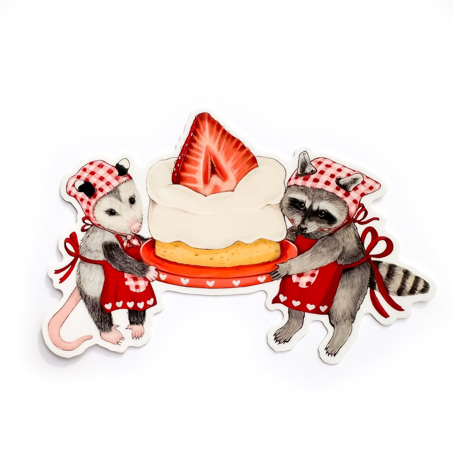 A weatherproof vinyl sticker of an opossum and raccoon in red heart aprons holding a strawberry shortcake on a red plate on a white background.