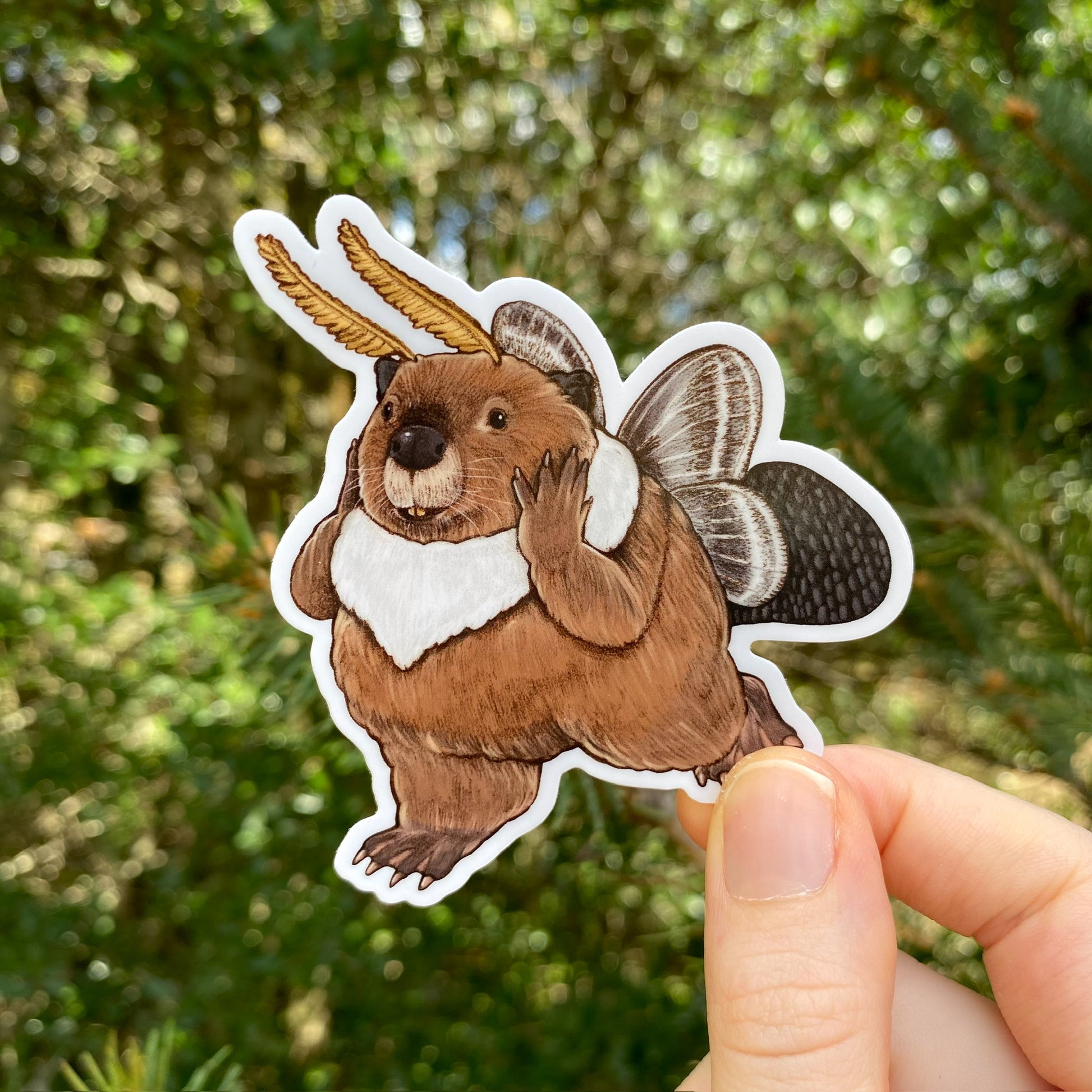 A hand holding a sticker of a beaver with Tolype moth wings.  