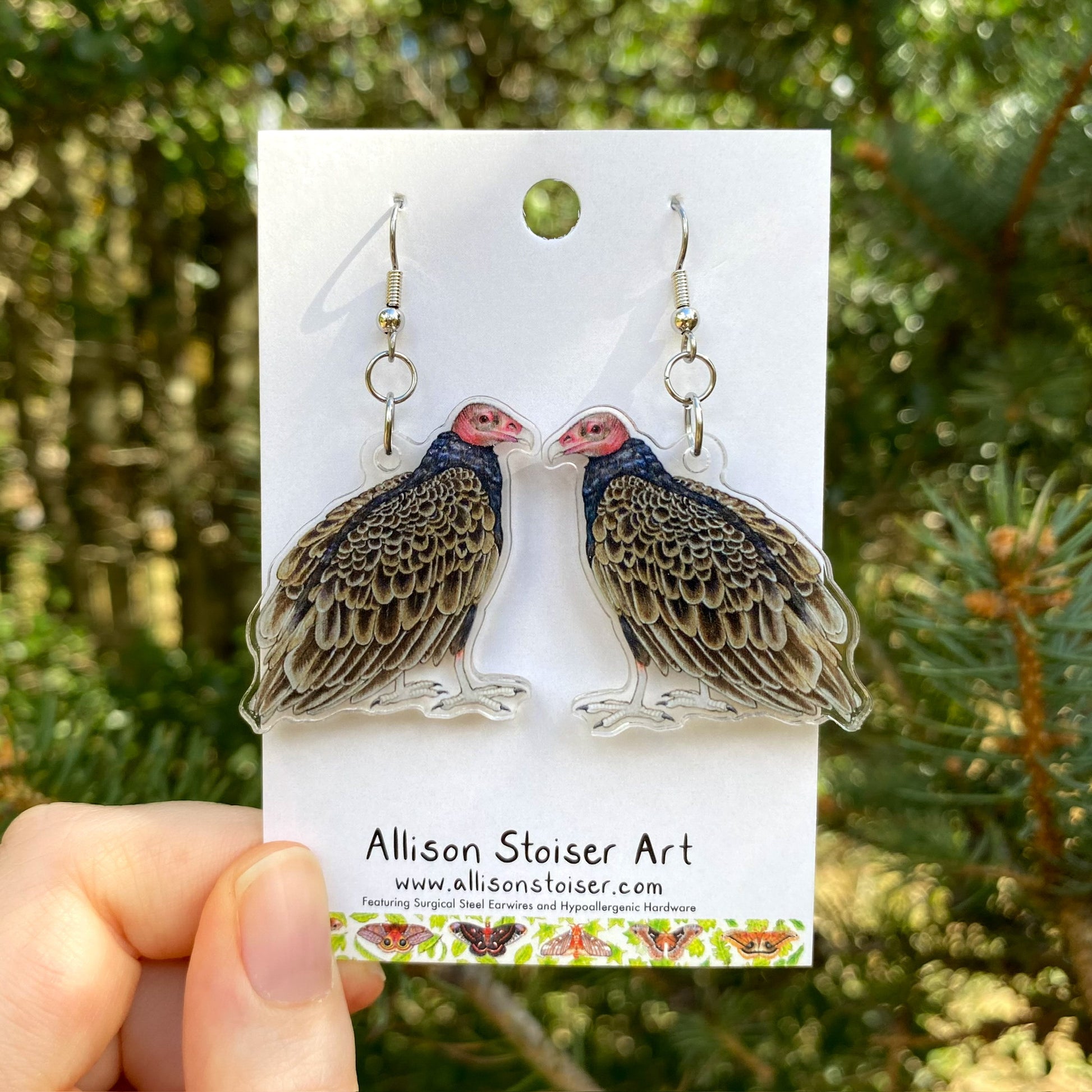 A hand holding a pair of turkey vulture earrings