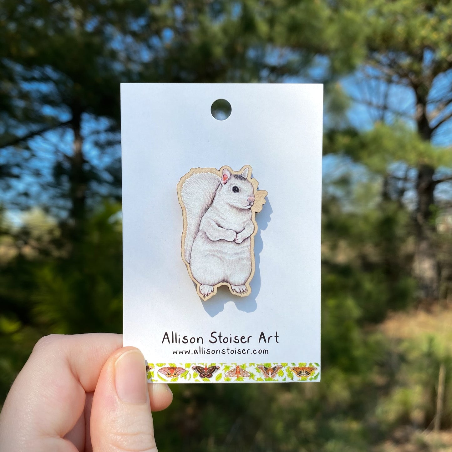 White squirrel wooden pin on a card held by a hand with a blurred natural background