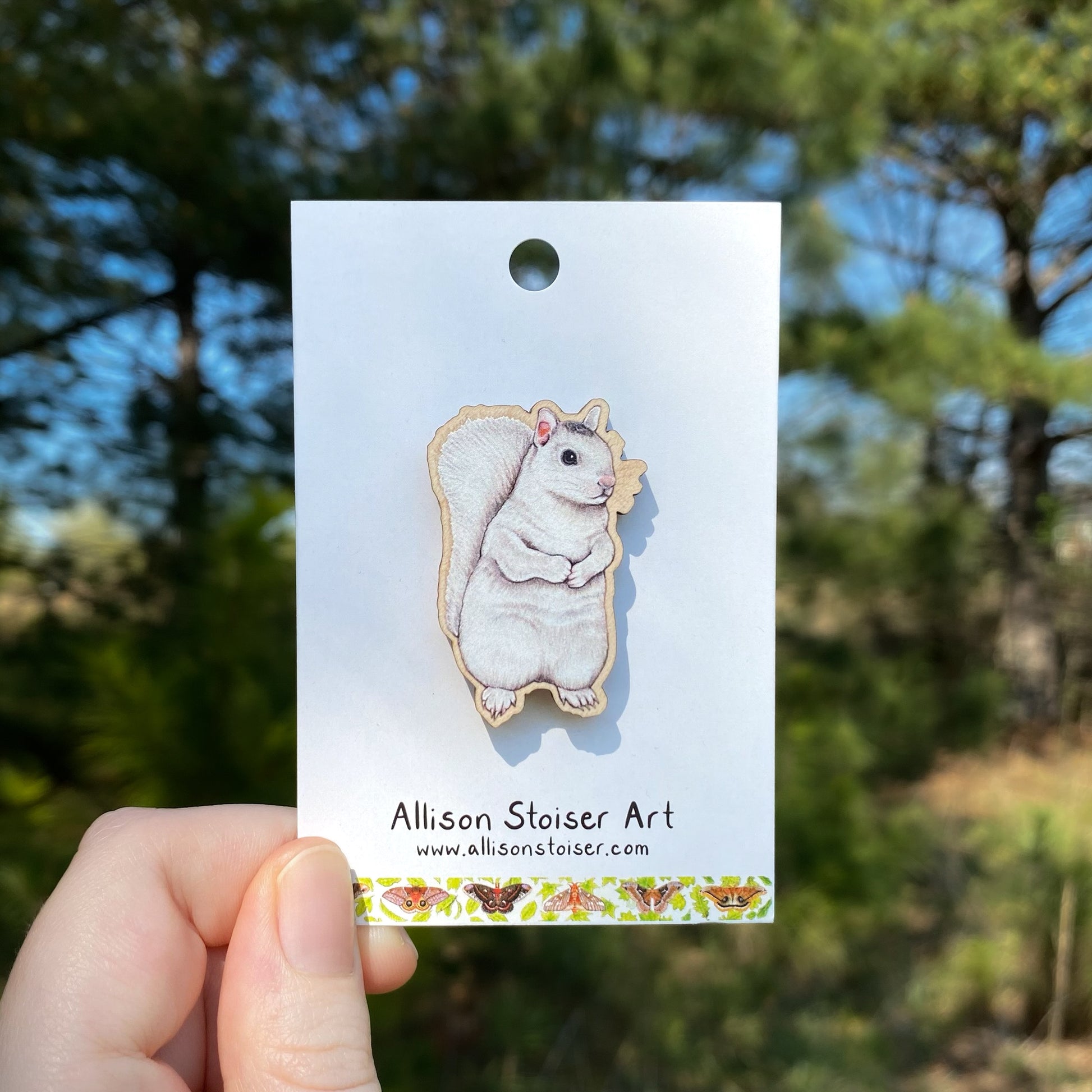 White squirrel wooden pin on a card held by a hand with a blurred natural background