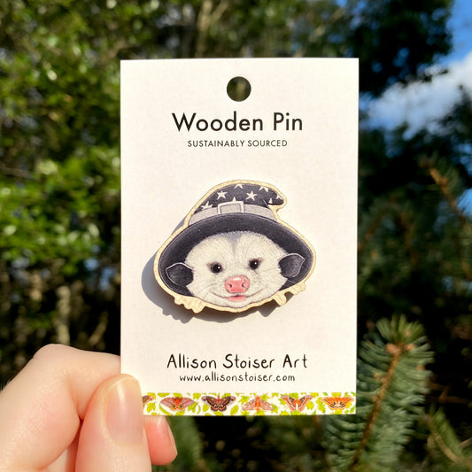 A wooden pin of an opossum in a wizard hat