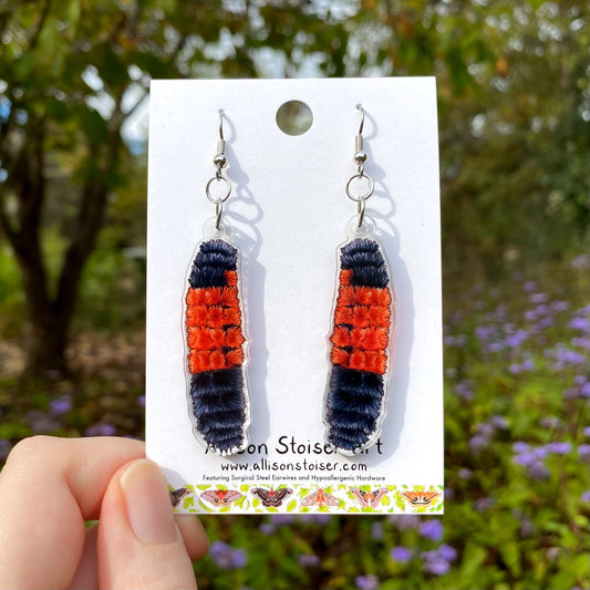 Pair of earrings of woolly bear caterpillars on a card held by a hand with a natural background