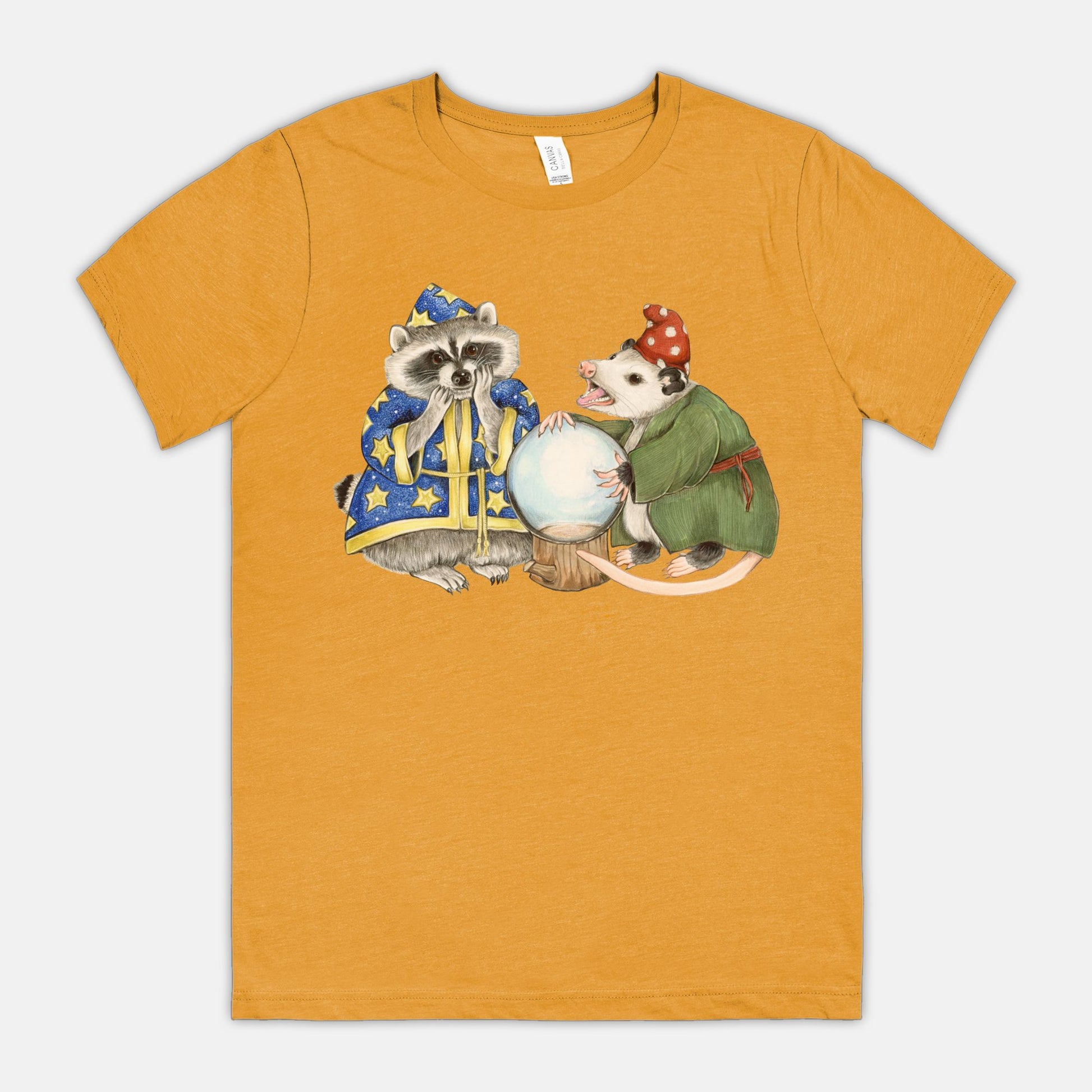 A mustard-colored t-shirt featuring an illustration of a raccoon wizard and opossum fortune teller