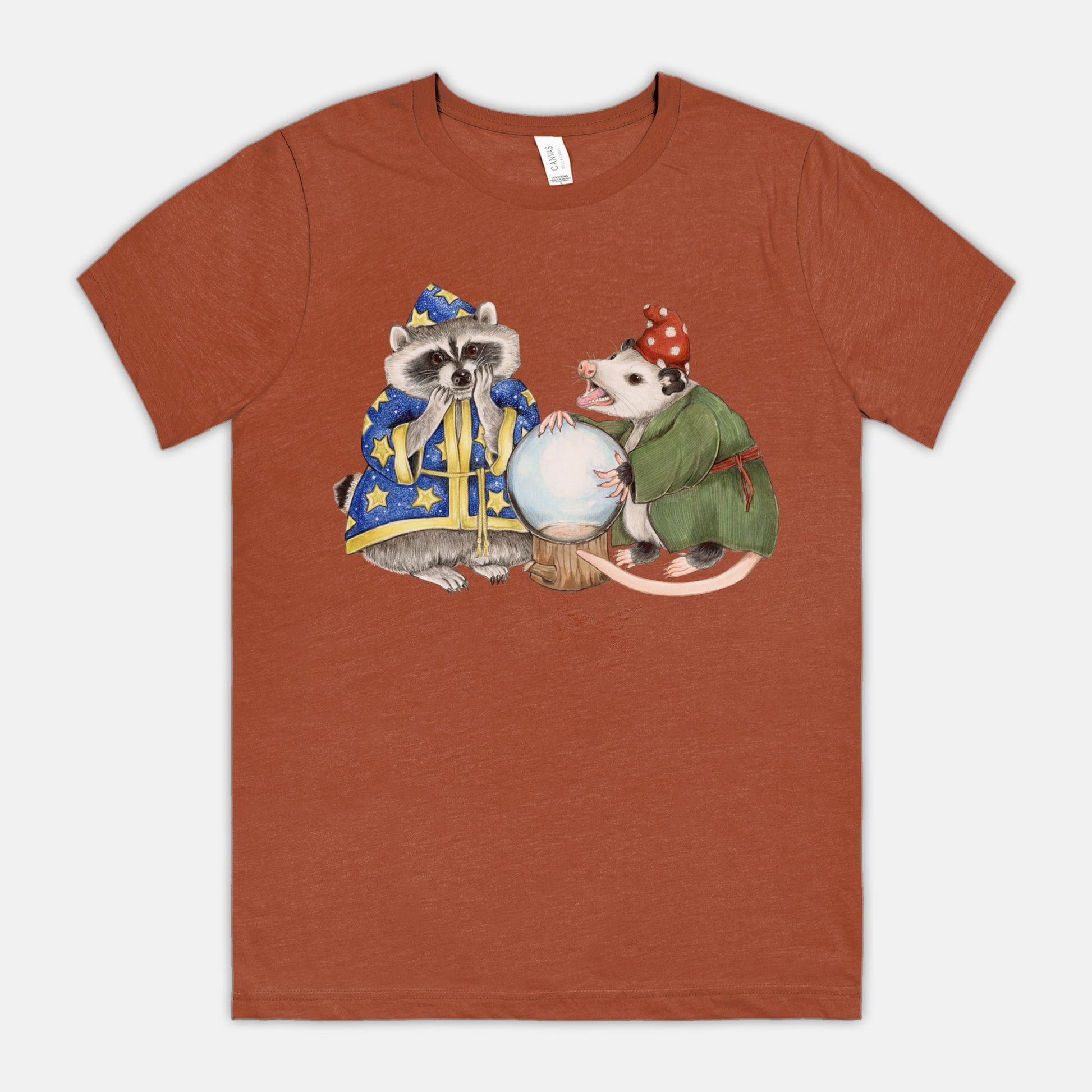 A dark orange t-shirt featuring an illustration of a raccoon wizard and opossum fortune teller