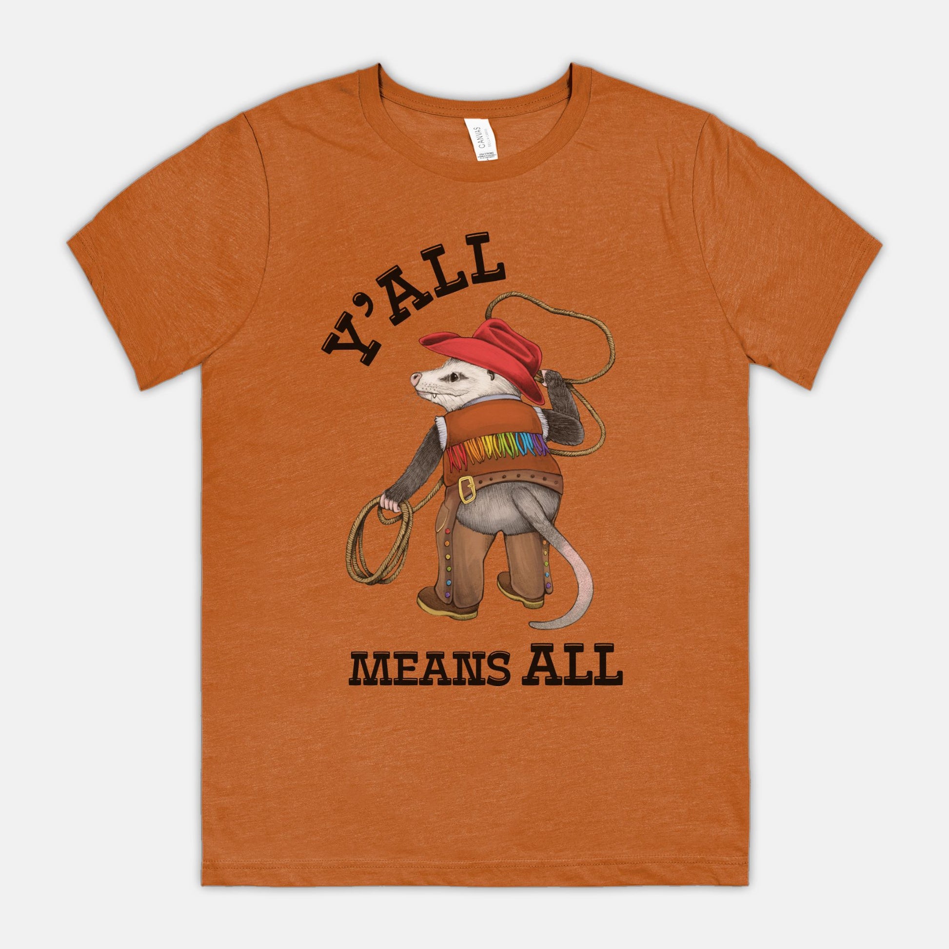 A dark orange-colored shirt featuring a cowboy opossum and text reading “Y’all Means All”