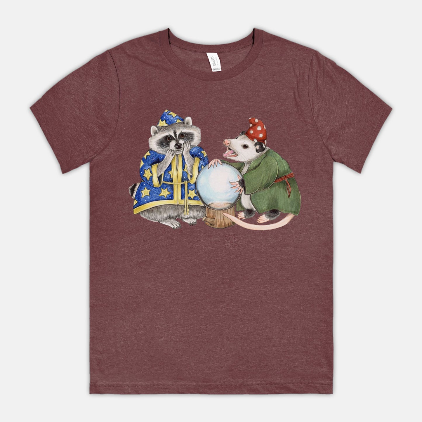 A burgundy t-shirt featuring an illustration of a raccoon wizard and opossum fortune teller