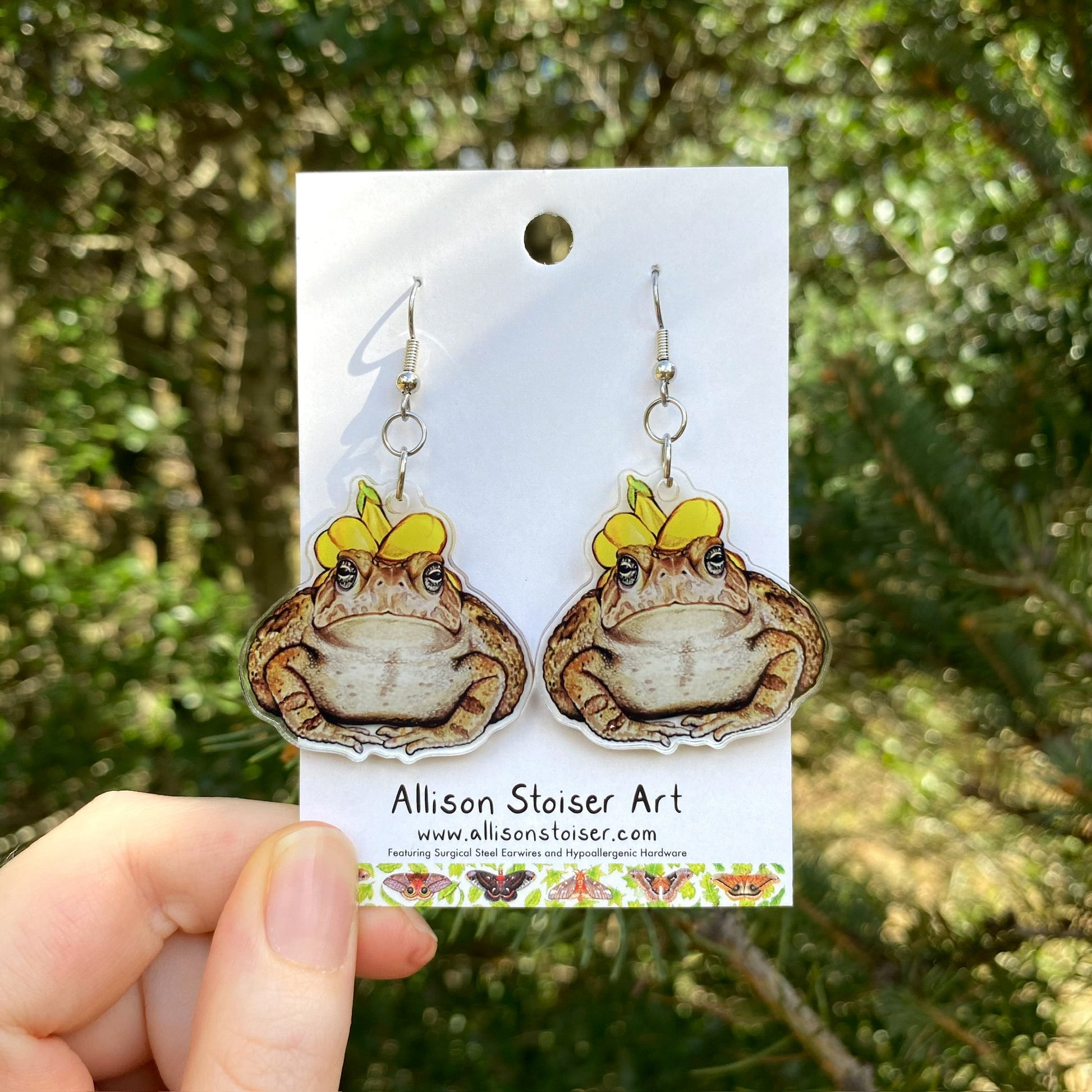 A hand holding a pair of flower hat toad acrylic earrings