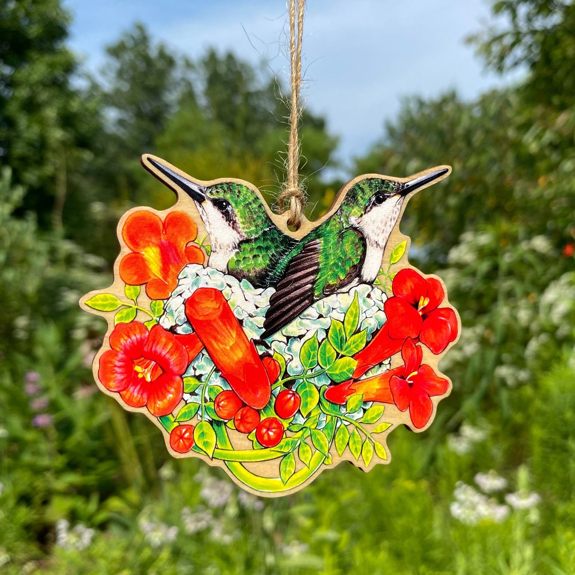 A wood print ornament featuring an illustration of hummingbirds in a nest