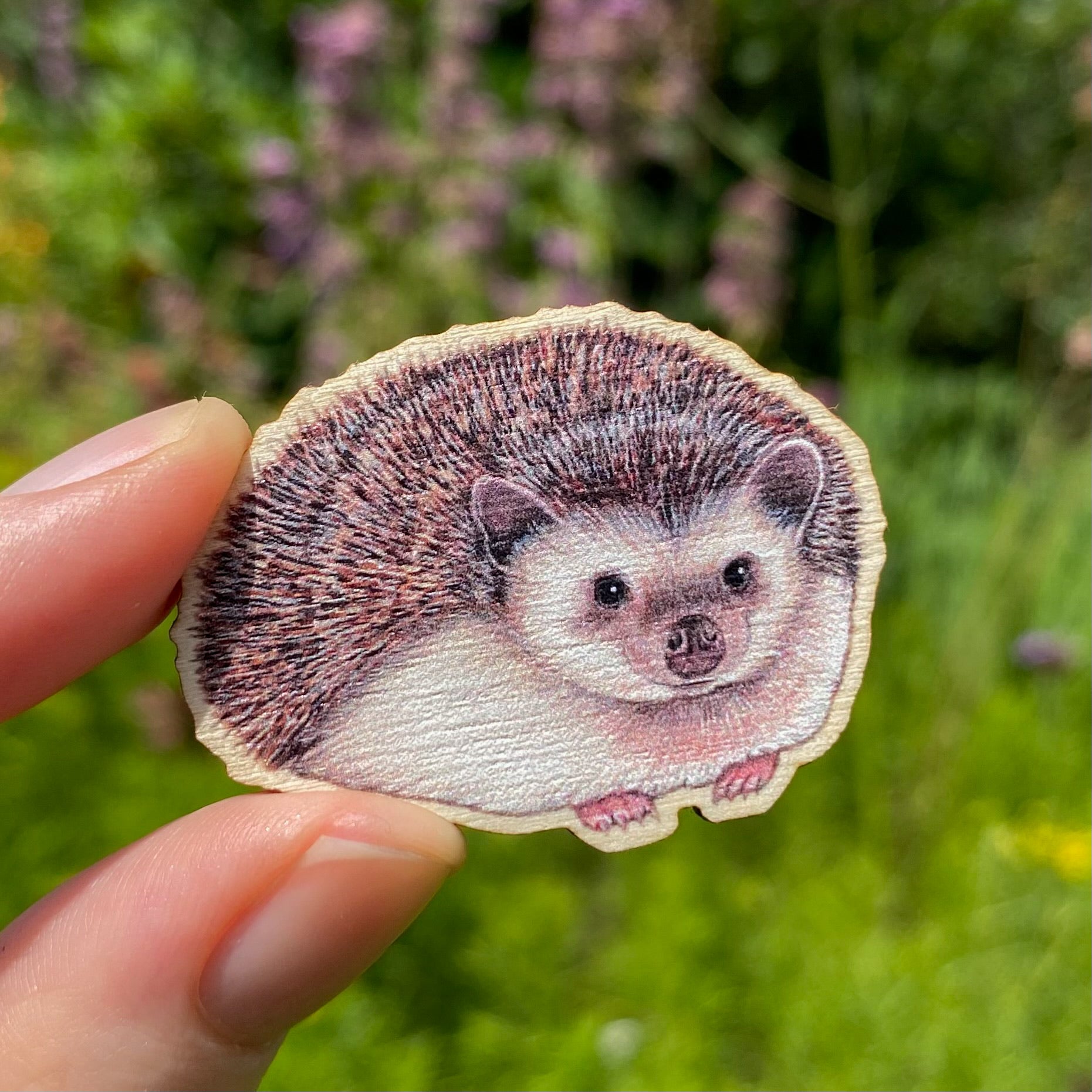 A hand holding a sustainably sourced wooden pin featuring an illustration of a hedgehog