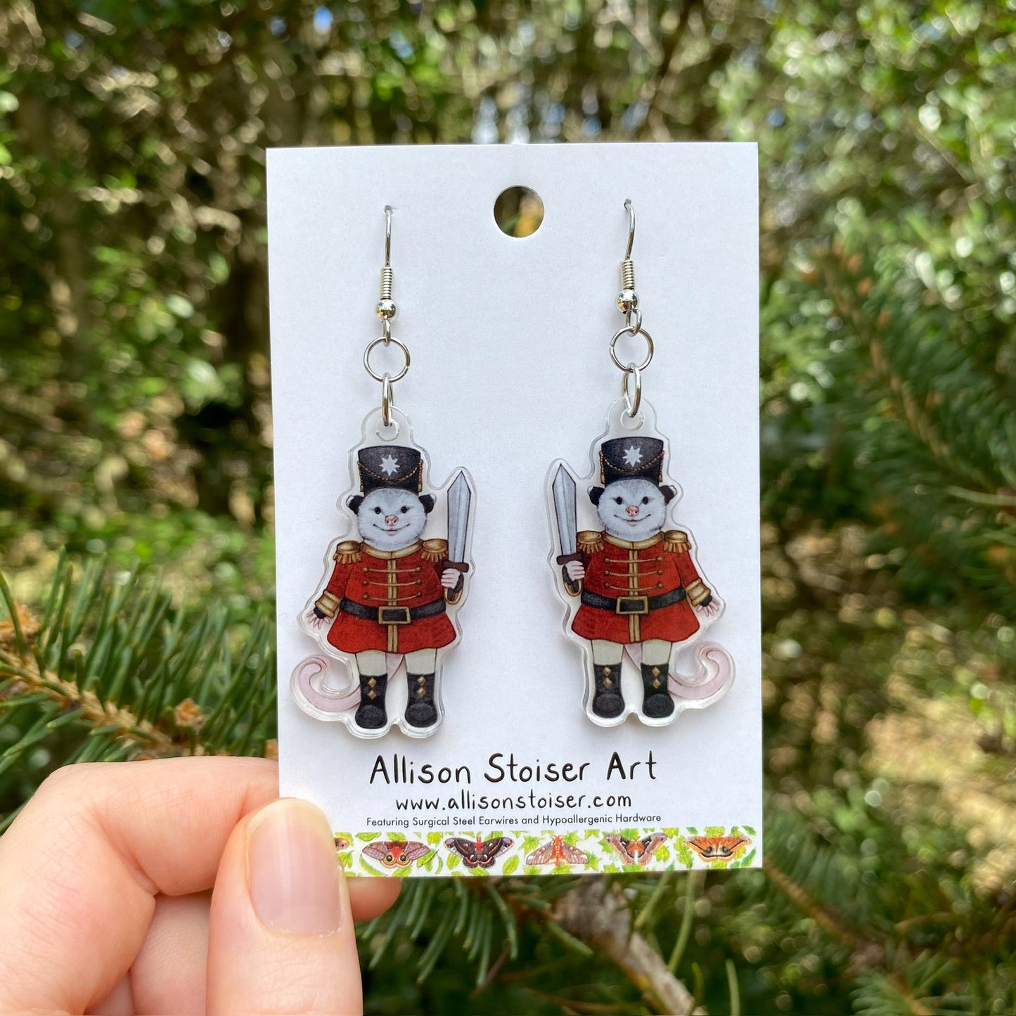 A hand holding a pair of opossum nutcracker acrylic earrings 