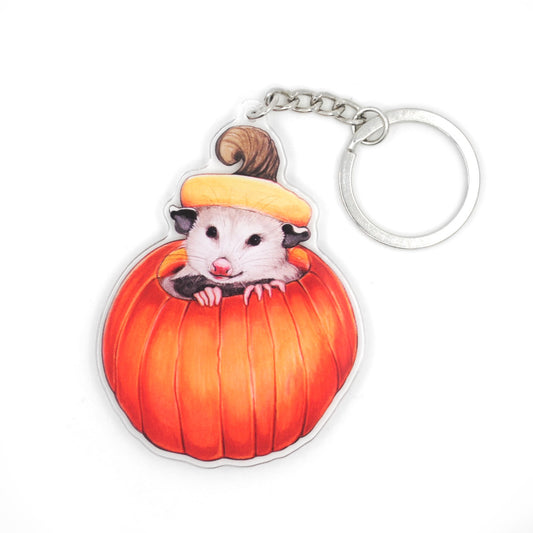 A keychain  featuring an opossum peeking up from a pumpkin