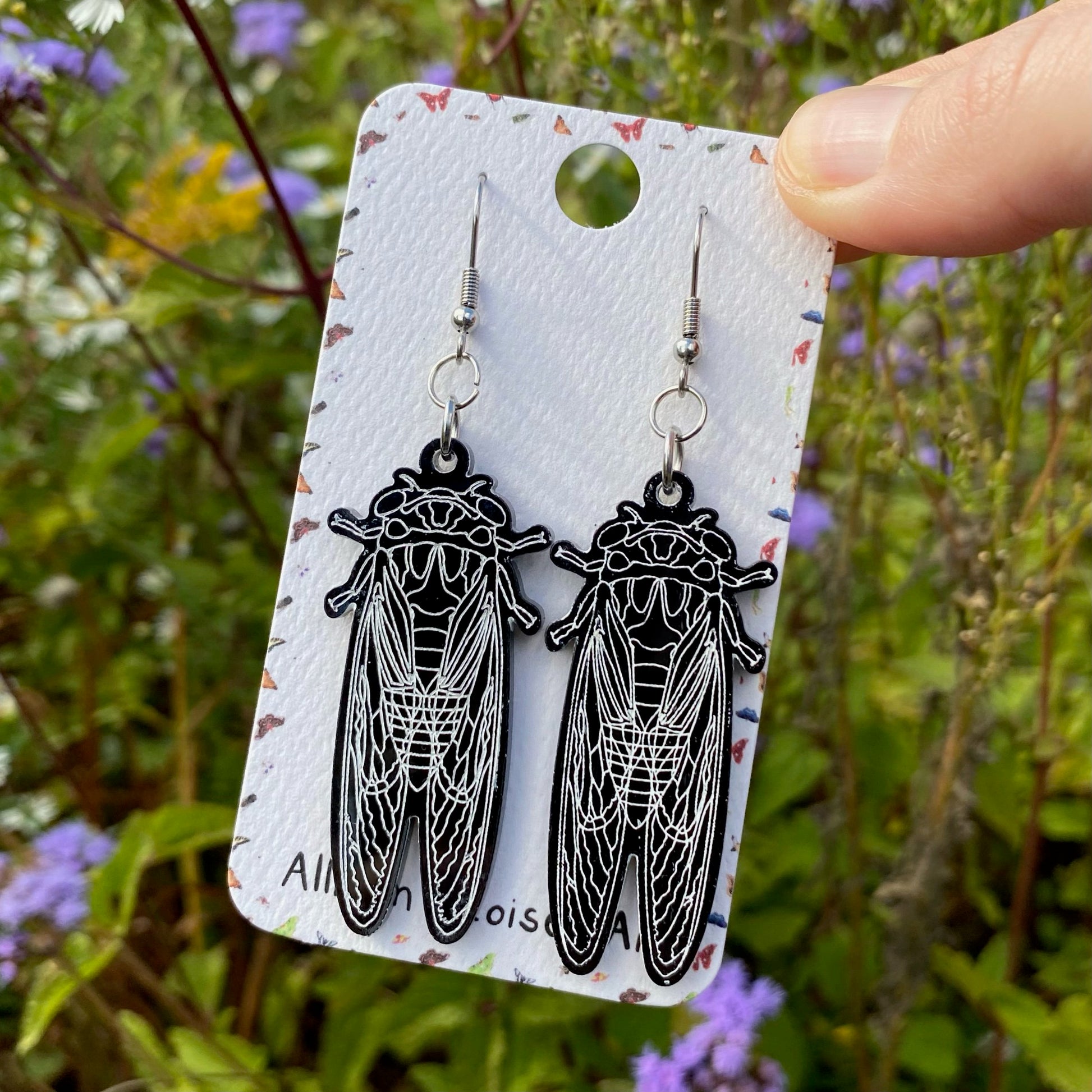 A hand holding a pair of black acrylic cicada earrings