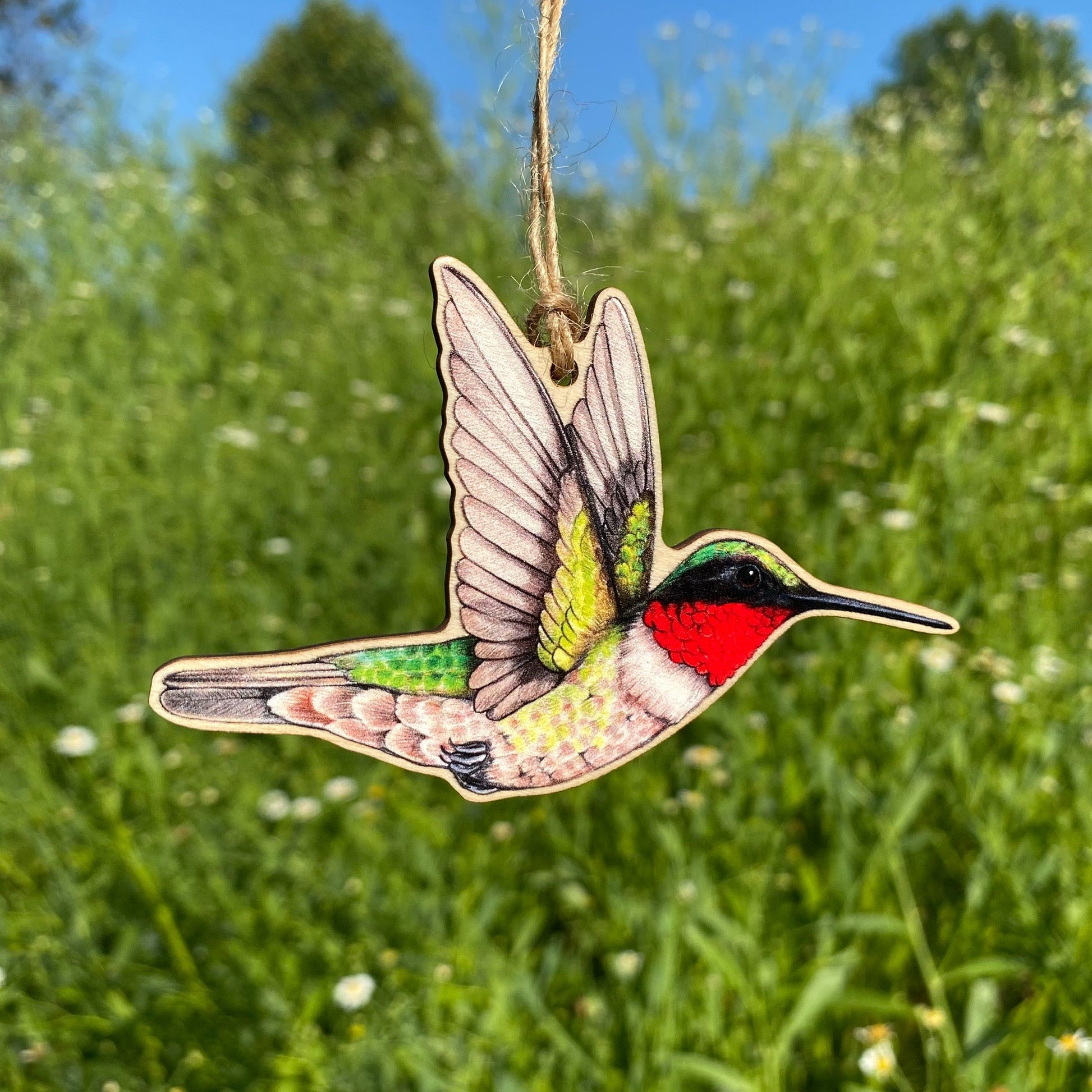 A wooden ornament strung with twine of a male ruby-throated hummingbird.