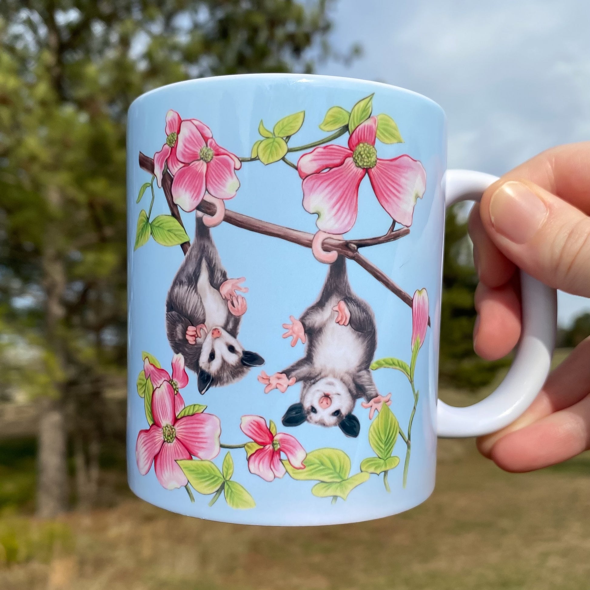 A mug featuring baby possums hanging upside down in dogwood