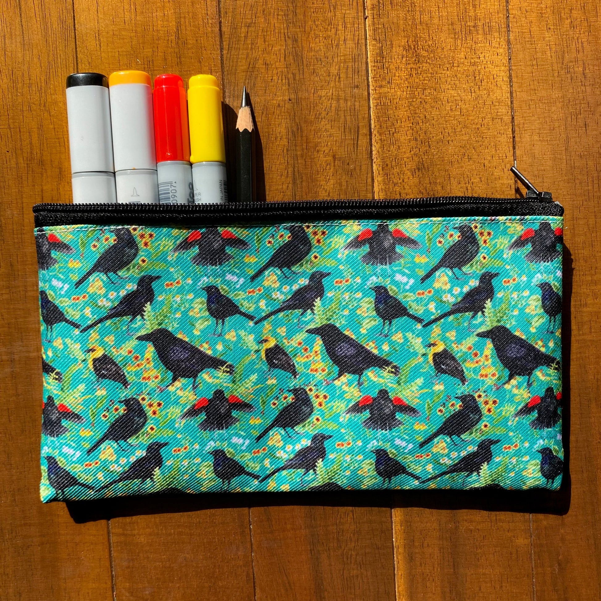 A teal zippered pouch featuring a pattern of crows and blackbirds