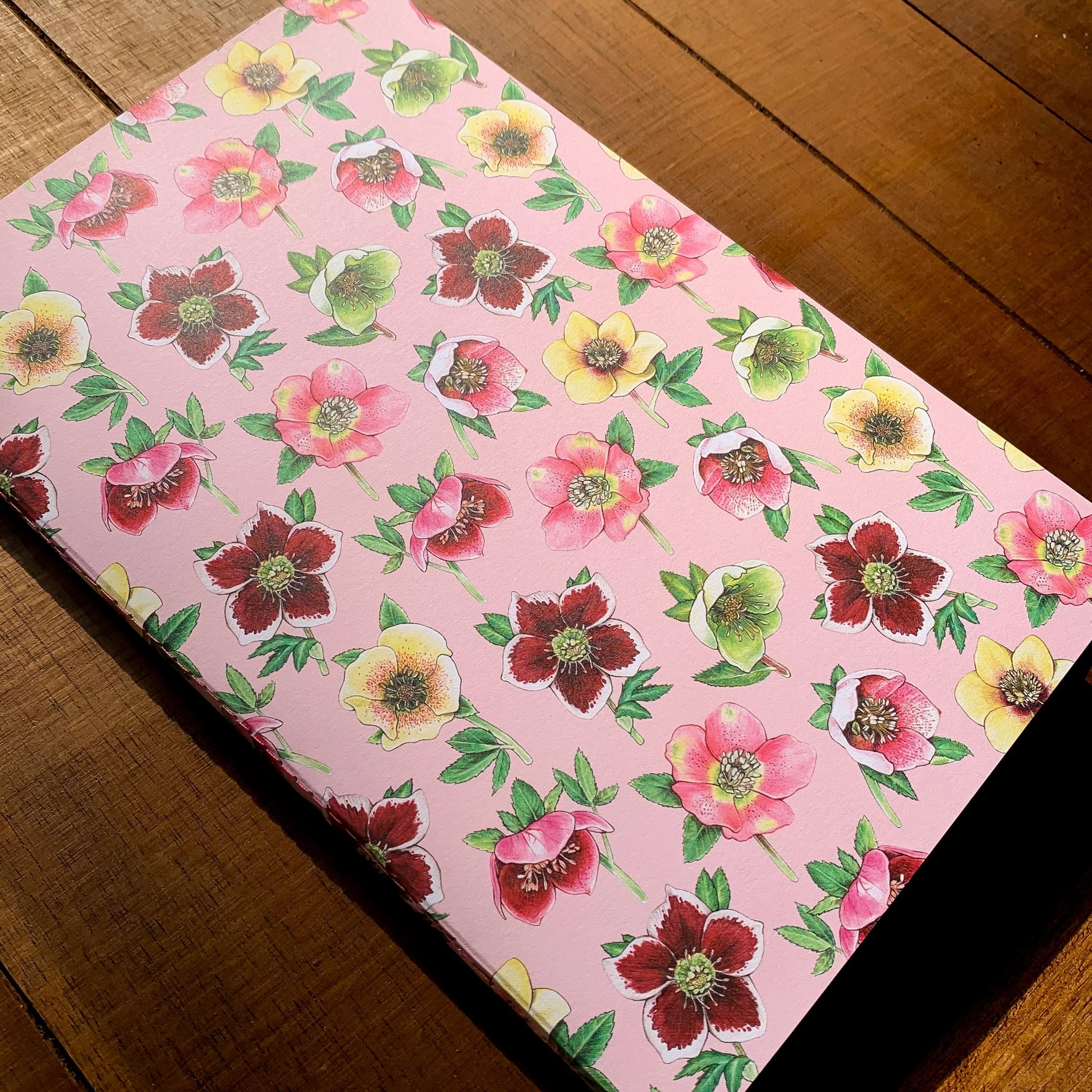 A handmade journal featuring a pattern of lenten roses on a pink background