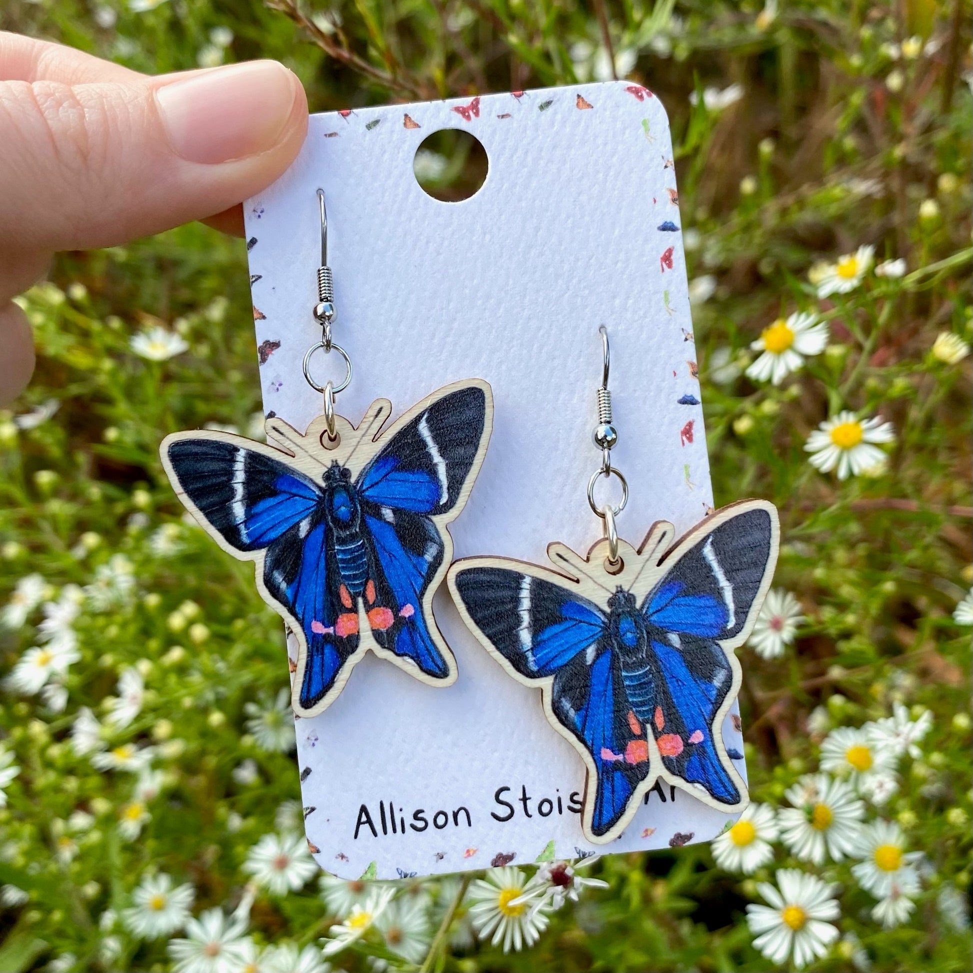 A hand holding a pair of periander metalmark earrings