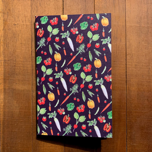 A handmade journal featuring a pattern of garden veggies on a purple background