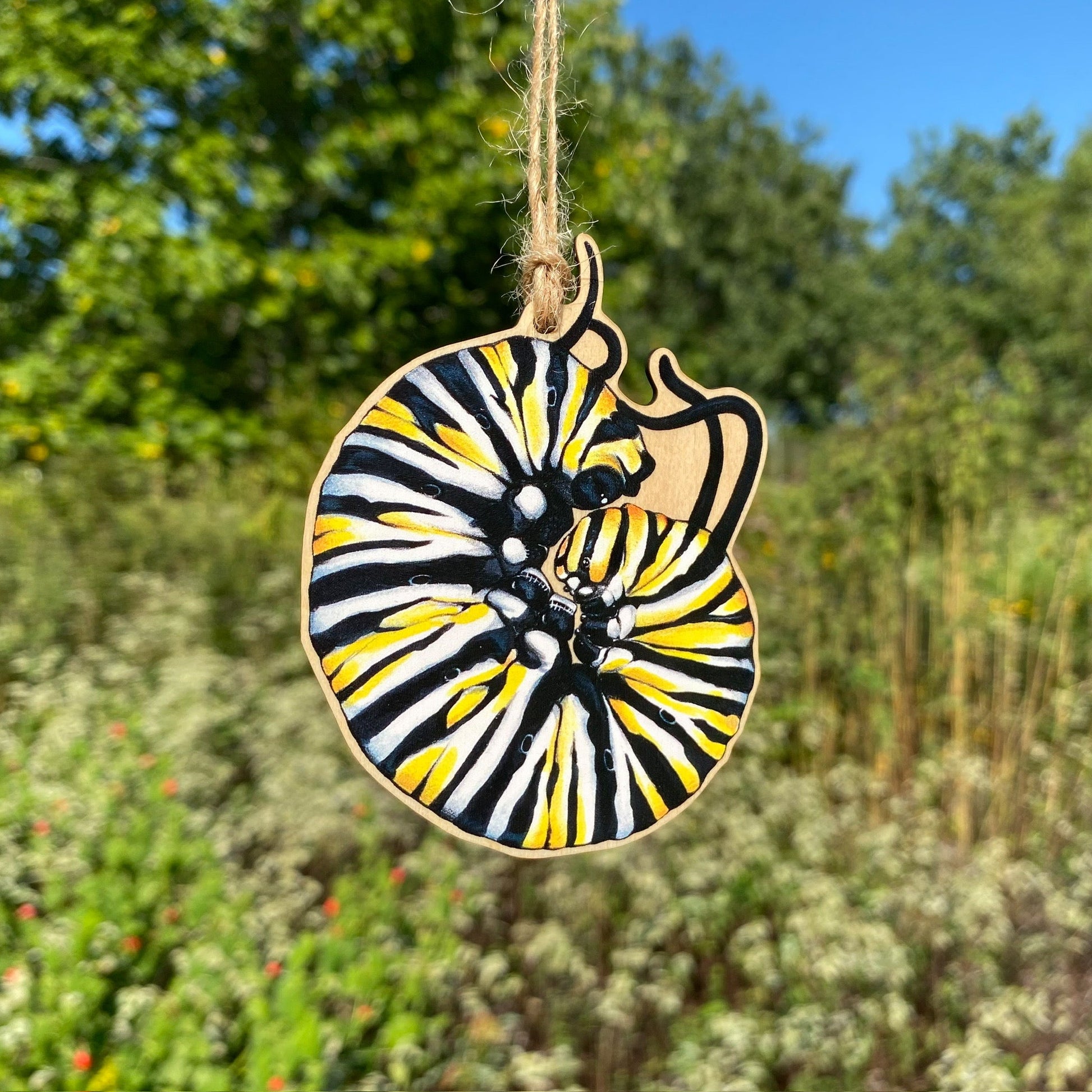 A wooden ornament strung with twine of a curled up monarch caterpillar.