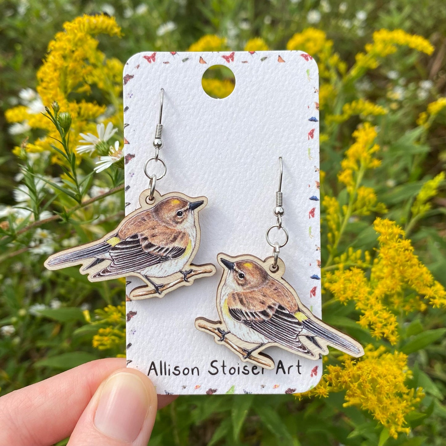 A hand holding yellow-rumped warbler earrings 