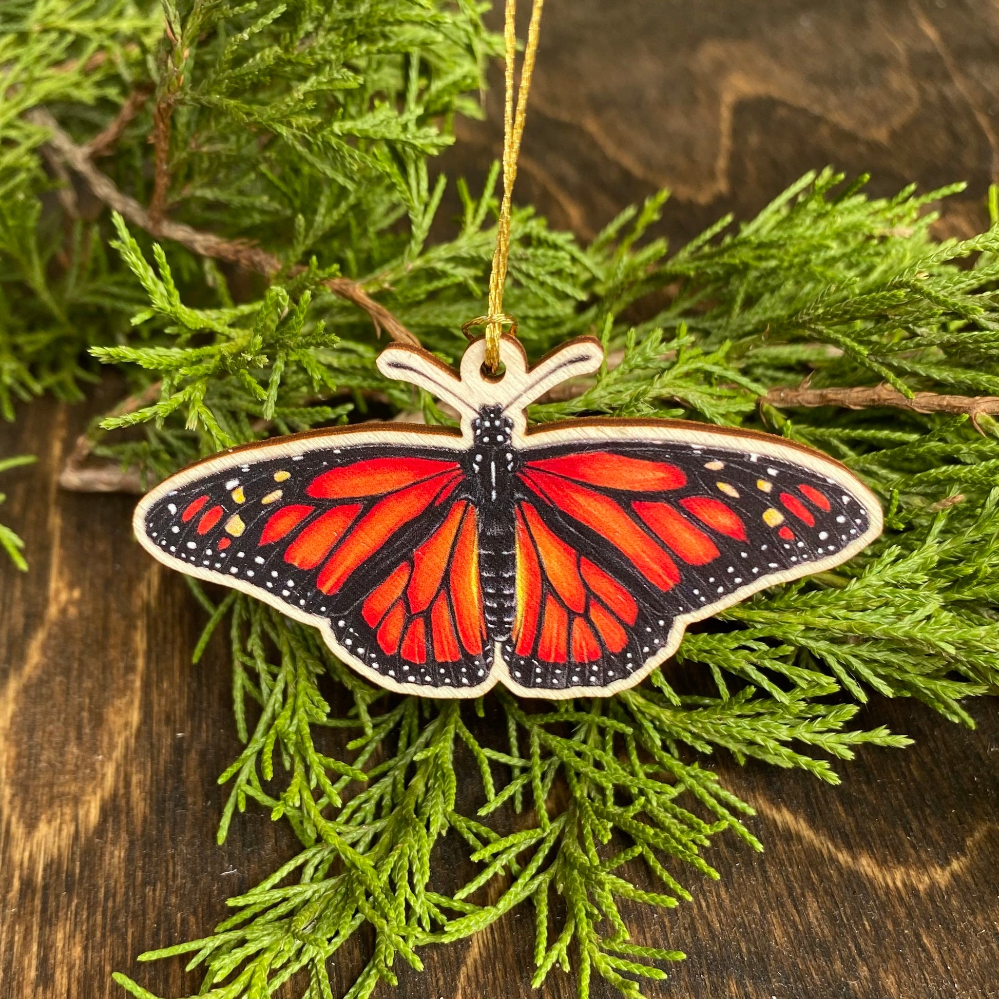 A small wood ornament strung up with gold string of a monarch butterfly.