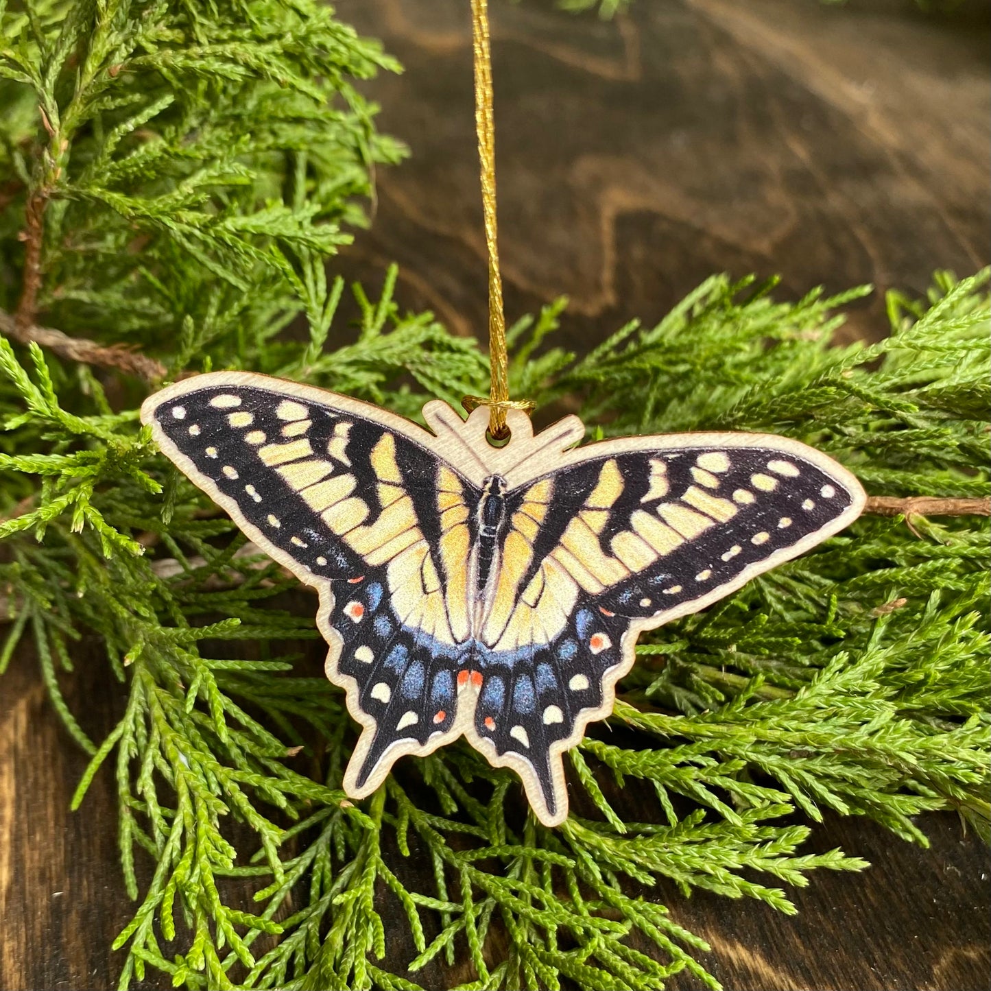 A small wood ornament strung up with gold string of a tiger swallowtail butterfly.