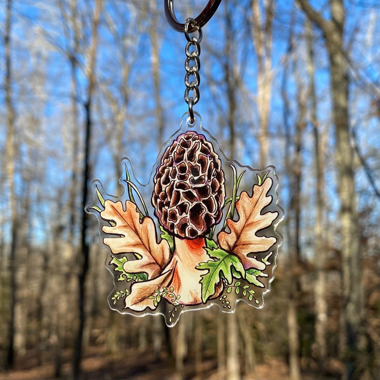 A keychain of a morel mushroom being held in front of the forest.