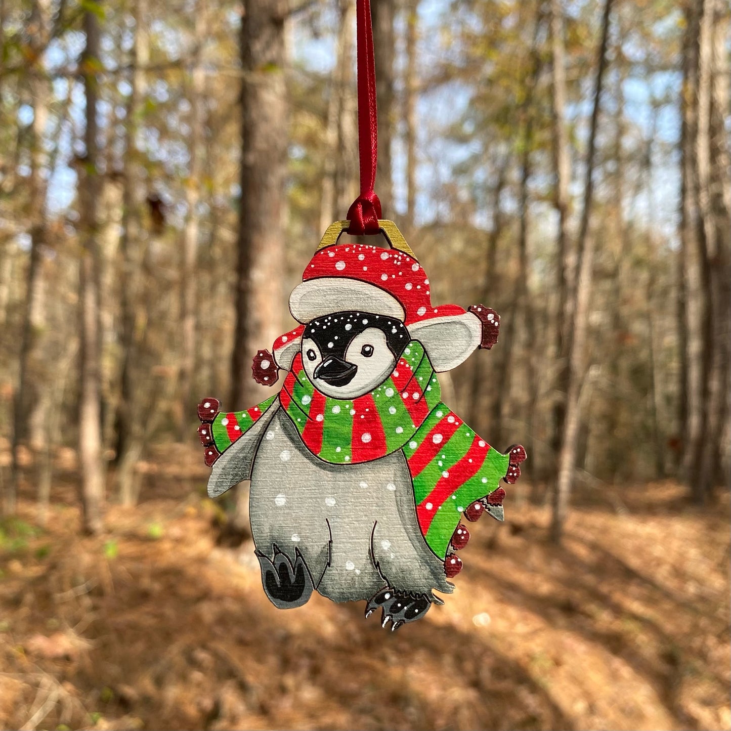 A hand-painted ornament of a penguin wearing a red hat and a green-and-red striped scarf